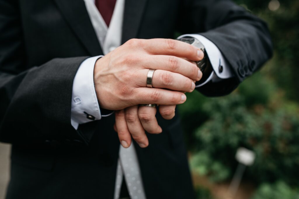 Man wearing a black suit and a gold ring checking the time on his watch